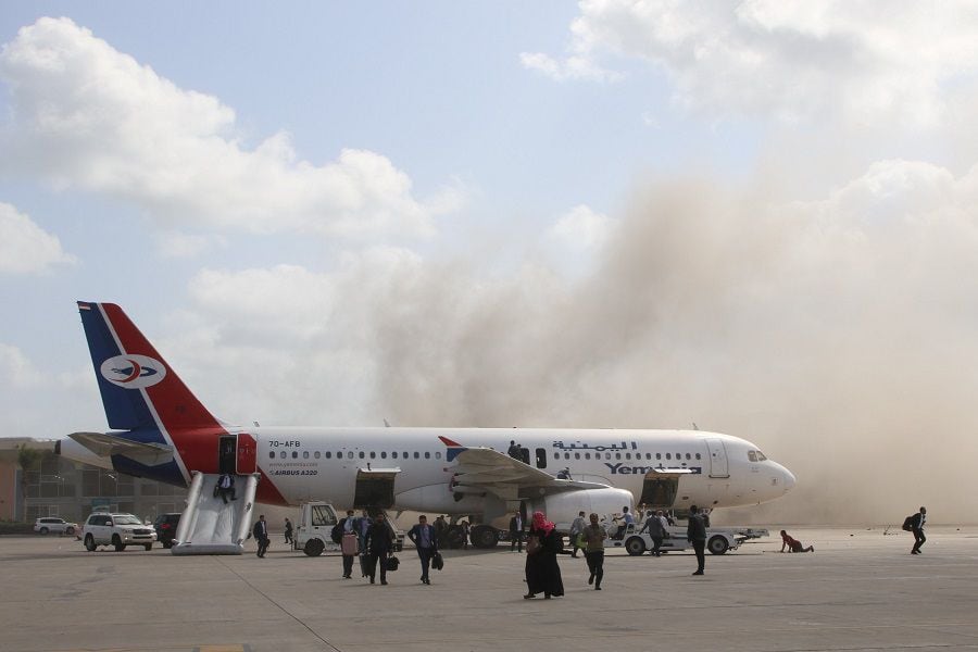 People walk on the tarmac as dust and smoke rise after explosions hit Aden airport, upon the arrival of the newly-formed Yemeni government in Aden