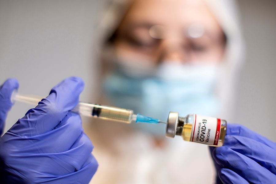 A woman holds a small bottle labeled with a "Coronavirus COVID-19 Vaccine" sticker and a medical syringe in this illustration