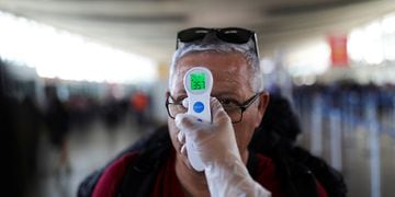 An employee takes the temperature of a man as a preventive measure against the coronavirus disease (COVID-19) in the Santiago's International airport, in Santiago