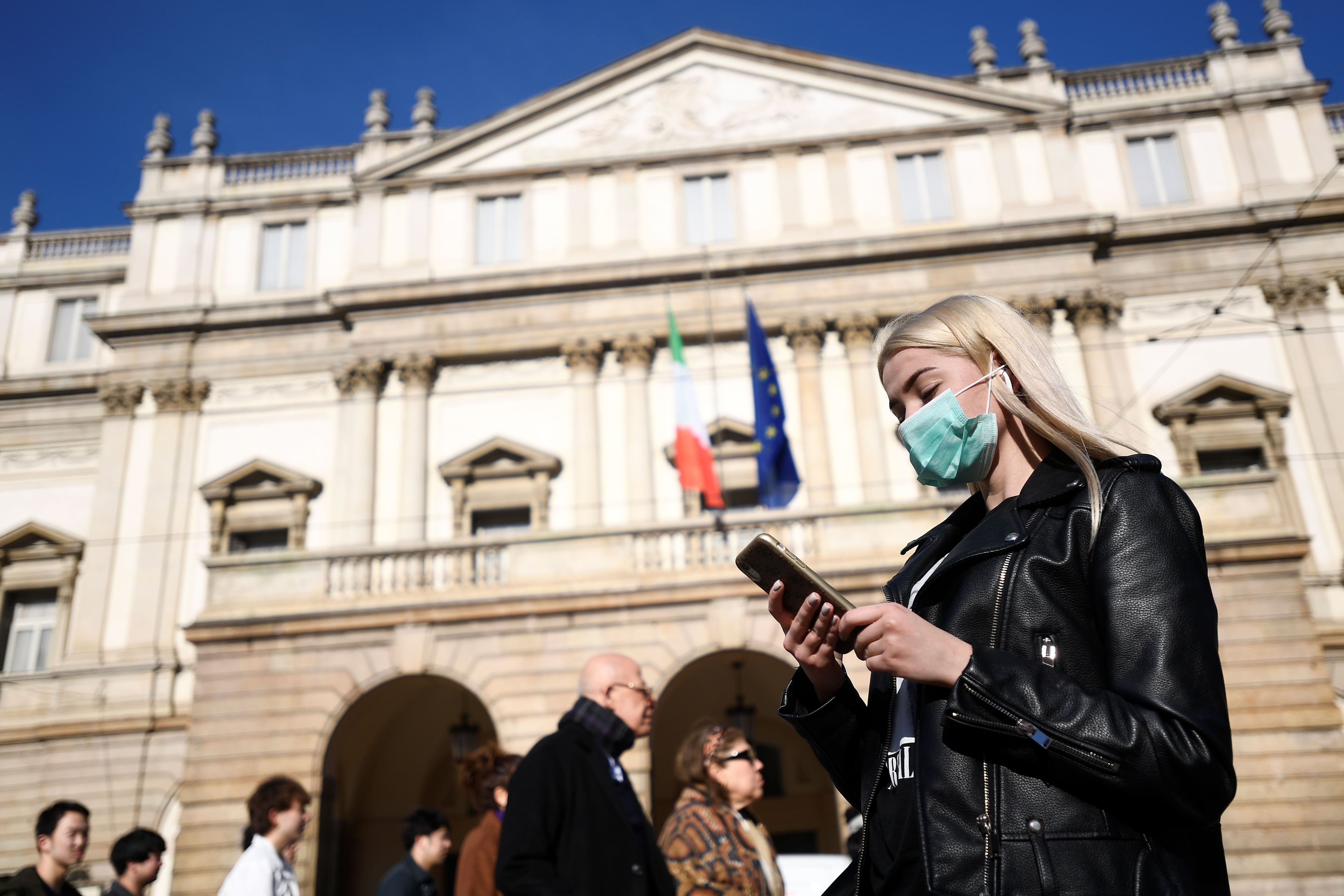 A woman wearing a face mask checks her phone outside the Teatro alla Scala in Milan