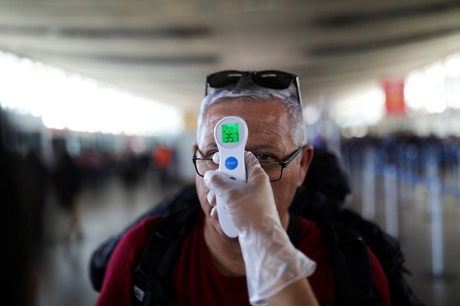 An employee takes the temperature of a man as a preventive measure against the coronavirus disease (COVID-19) in the Santiago's International airport, in Santiago