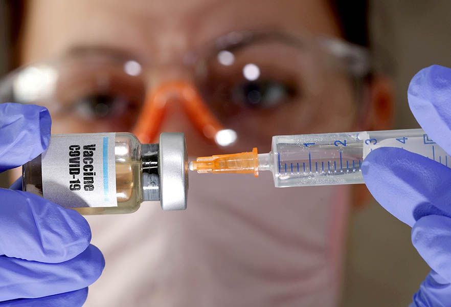 FILE PHOTO: A woman holds a small bottle labeled with a 'Vaccine COVID-19' sticker and a medical syringe in this illustration